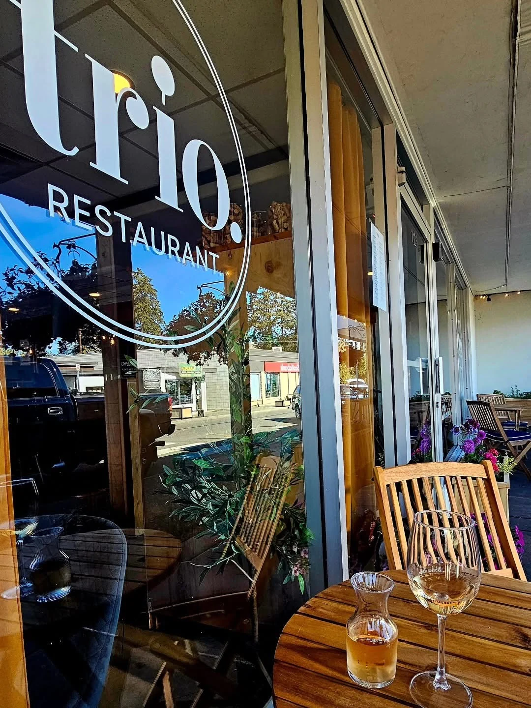 Trio Restaurant lettering on the storefront window beside outdoor wooden tables