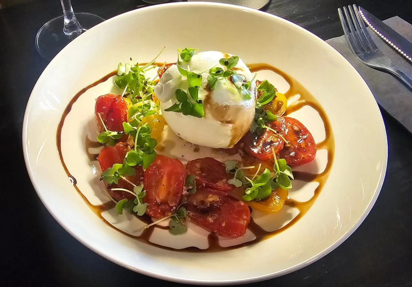Burrata, colourful tomatoes and fresh greens served on a white plate