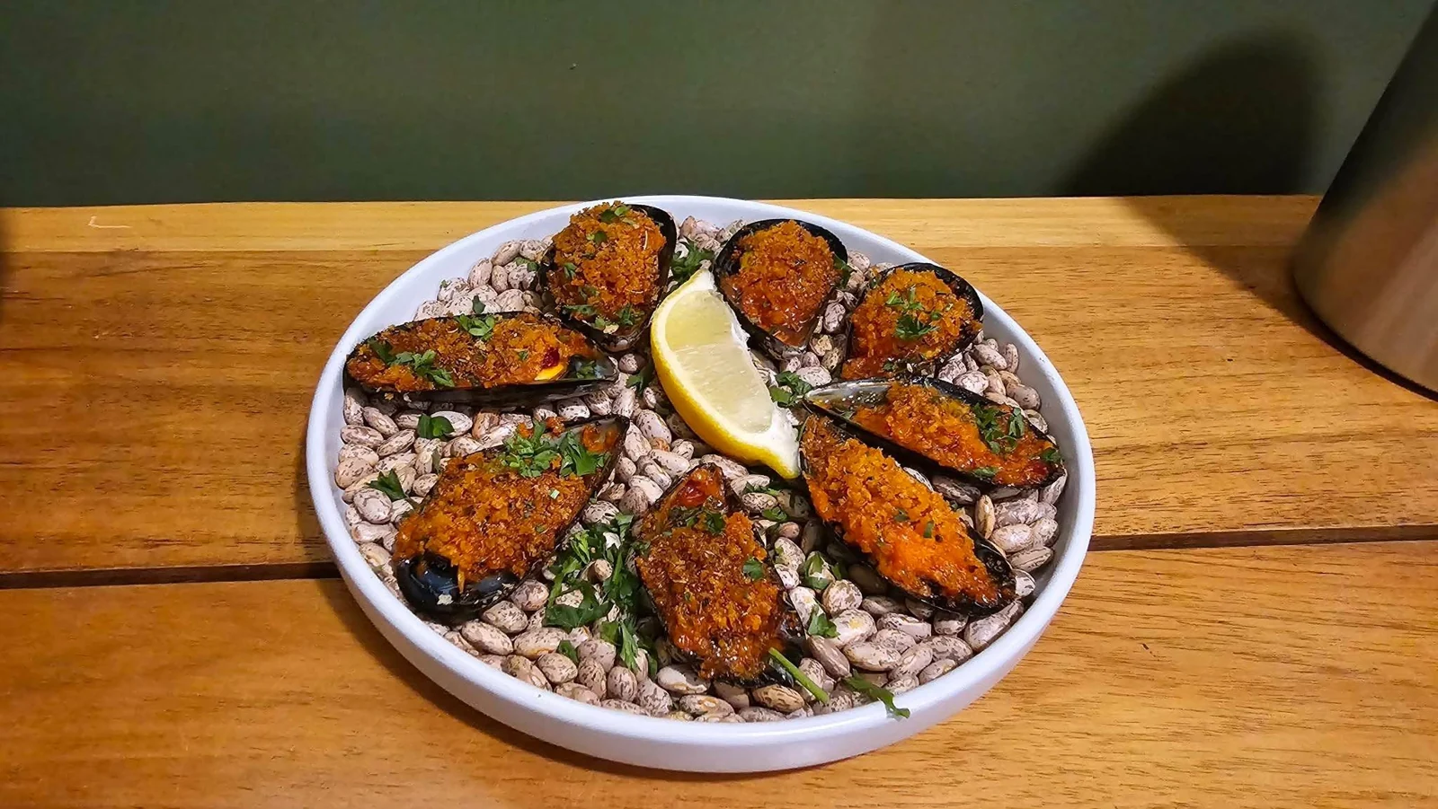 Mussels in their shells with a browned topping and lemon wedges