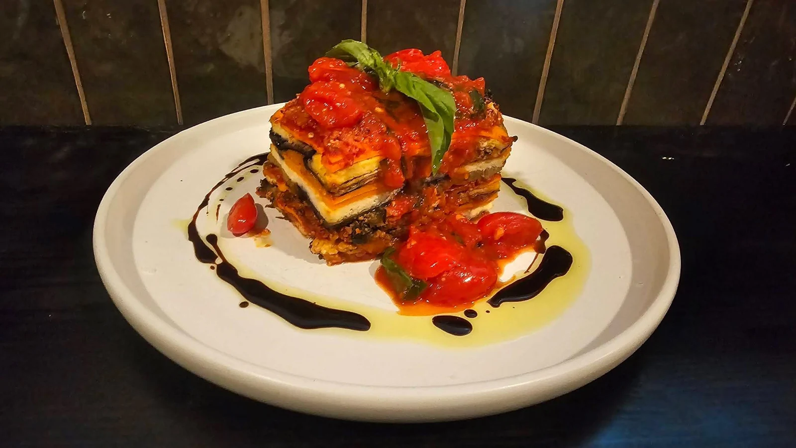 A layered dish with red sauce and basil on a white plate
