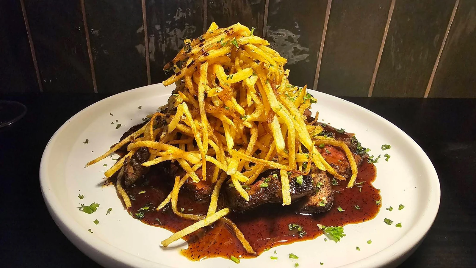 A plated meat dish topped with a tall pile of thin fries