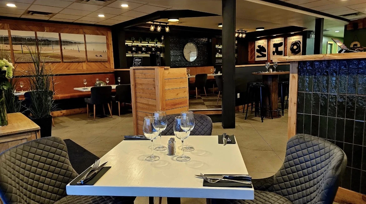 Trio’s dining room with white tables, quilted dark chairs, warm wood and amber seating